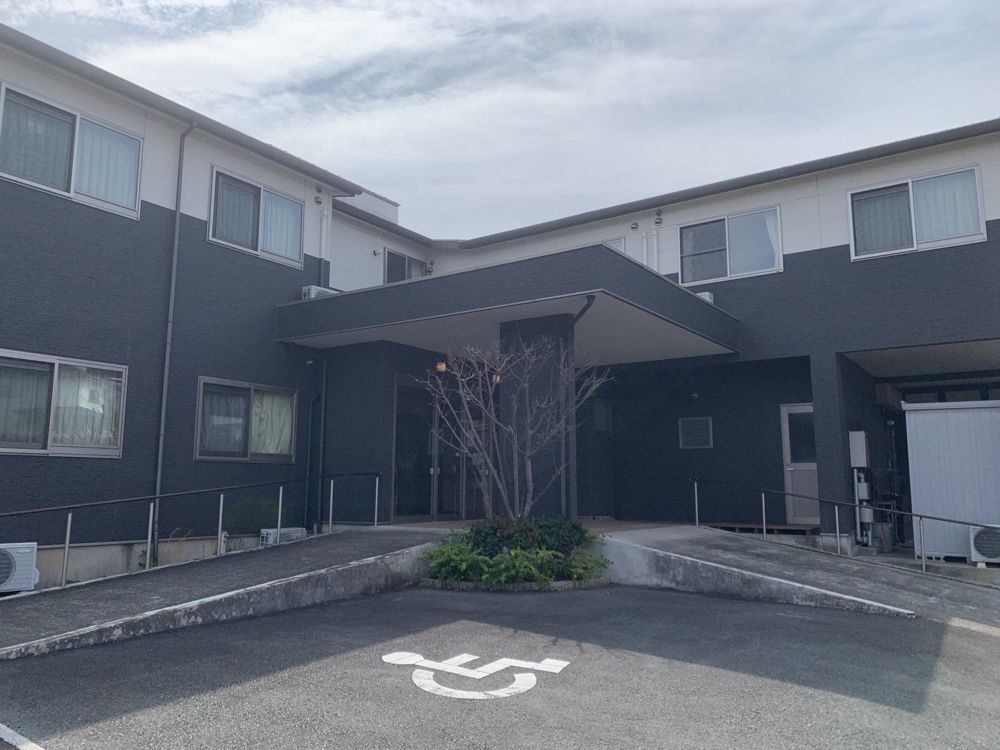 紺色の2階建ての建物と、車いす用の駐車区画のある正面