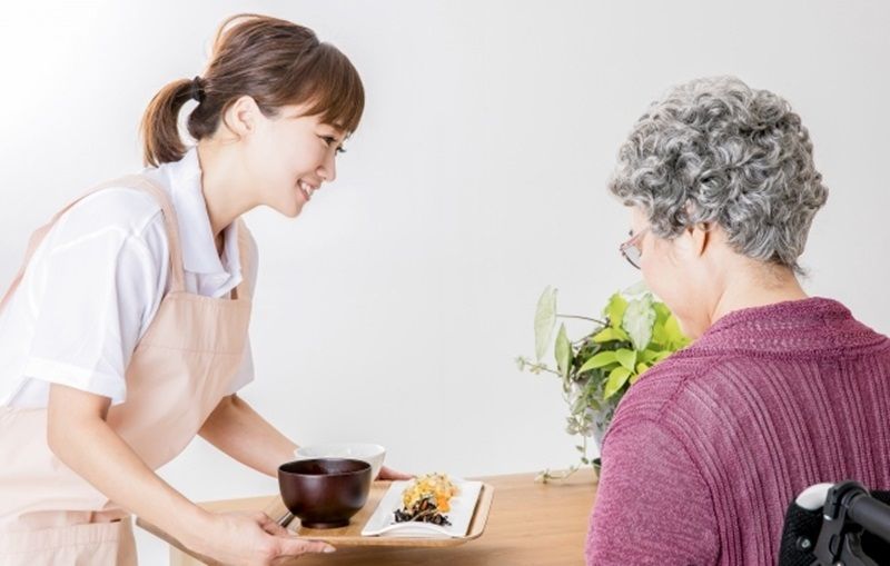職員が高齢の女性のテーブルへ食事を運んでいる