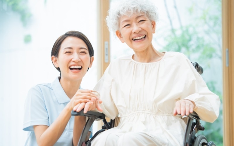 車いすの高齢の女性と並んで、手を添えてほほえむ職員