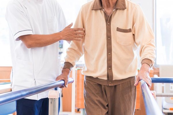 手すりにつかまって歩く練習をする高齢の男性と職員
